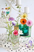 Romantic, still-life arrangement of colourful wildflowers in various glasses on polka-dot fabric