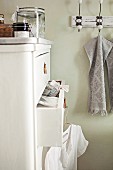 weiße Landhaus-Kommode mit leicht geöffneter Schublade und Vintage Hakenleiste auf lindgrüner Badezimmerwand