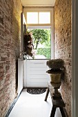 Plant in antique urn on rustic bench in narrow hallway with exposed brick walls leading to stable door with open top half