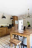Esstisch und Hocker aus Massivholz, gegenüber Küchenzeile in ländlicher Küche mit Terrakottaboden