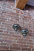 Oriental lanterns hanging from wooden beam against brick wall