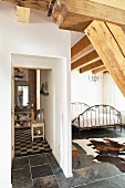 Bathroom with chequered floor adjoining open-plan bedroom with metal bed and cowhide rug on slate floor