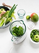 Mixer mit frischen Spinatblättern, rundherum grüne Früchte und grünes Gemüse
