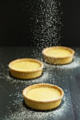 Lemon tarts being dusted with icing sugar