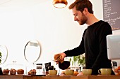 Junger Angestellter im Café giesst Filterkaffee in Kaffeetassen