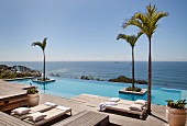 Loungers on wooden deck and palm trees in infinity pool with sea view