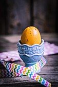 Gelb gefärbtes Ei in Keramik-Eierbecher mit Geschenkband