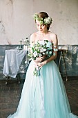 Fairy-tale bride holding bouquet and wearing flower wreath in vintage interior