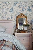Vintage ornaments on bedside table against wallpaper with vintage-style floral pattern