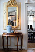 Antique, semicircular console table below gilt-framed mirror on wall next to open door