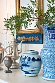Antike Silberkannen, blau-weisses Porzellangefäss und chinesische Vase auf Ablage vor Goldrahmenspiegel