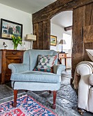 Antiker Sessel mit hellblauem Bezug, vor rustikaler Holzwand aus Bohlen, Blick durch offene Tür in Gangbereich