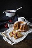 A sliced redcurrant Bundt cake dusted with icing sugar on a piece of white paper on a dark slate surface