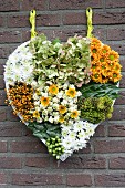 Hand-made, heart-shaped arrangement of chrysanthemums, hydrangeas and berries hung on brick wall