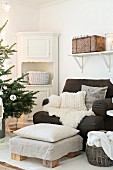 Fur blanket and cushions on comfortable armchair, footstools, corner cabinet and branches of Christmas tree