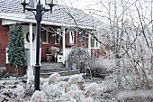 Backsteinhaus mit Veranda im winterlichen Garten mit Raureif