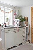 Mixer and vase of fir branches on festively decorated kitchen counter below garland of gingerbread hearts