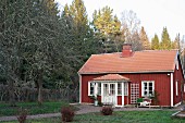 Blick vom Garten auf rotbraun gestrichenes Holzhaus mit weissen Fenstern