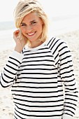 A blonde woman on the beach wearing a black and white striped, long-sleeved T-shirt