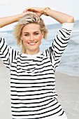 A blonde woman on a beach wearing a black and white striped, long-sleeved T-shirt