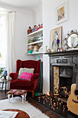 Red velvet armchair next to antique open fireplace decorated with fairy lights