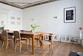 Antique, wooden chairs and dining table in dining room with gallery of pictures on floor