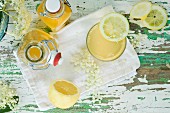 Bottles of elderflower syrup and a glass of elderflower cordial with a slice of lemon