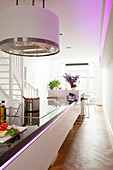 Modern island counter with integrated induction hob below cylindrical extractor hood lit by pale purple LED lights