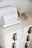 Index cards in transparent plastic box on top of wooden filing cabinet with leather handles