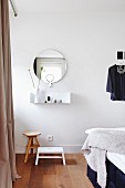 Minimalist wall-mounted shelf below round mirror above stools in bedroom