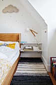Kinderzimmer unter dem Dach mit Holzgestellbett, Regalablagen als Nachttisch und schwarz-weißem Teppichläufer