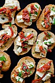 Bruschetta topped with feta cheese, dried tomatoes and herbs (seen from above)