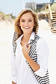 A young woman on a beach wearing a white top and a stripy knitted sleeveless jacket with a hood