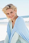 Blonde Frau in hell mintfarbenem Wollpulli und hellblauem Pulli um die Schultern am Strand