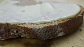 Eine Scheibe Graubrot mit Butter bestreichen (Close Up)