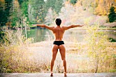 Rückansicht von sehr muskulöser Frau bei Gymnastik am See, nur mit Panty bekleidet