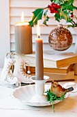 China candlestick with bird figurine, ice-skate ornament, stacked books and Christmas bauble hanging from sprig of holly