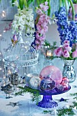 Baubles on glass cake stand in front of flower arrangement of hyacinths and roses in mercury silver vase