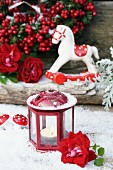 Small candle lantern and rose in artificial snow in front of rocking horse ornament and winter berries