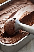 Chocolate ice cream in a container with an ice cream scoop (close-up)