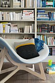A sofa cushion with a knitted cover in a bucket chair in front of a bookshelf