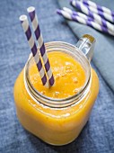 Exotic, yellow fruit smoothie in a glass jar with paper straws