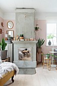 Kamin aus Beton mit verchromten Türen, Beistelltische mit Blumentöpfen vor rosa getönter Wand