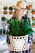 Woman wearing straw hat holding foliage plant in decorative pot
