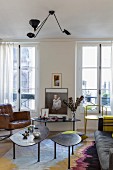 Retro pendant lamp with cantilever arms above set of coffee tables with amorphous tops and various seating in front of windows