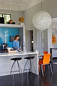 Woman at counter with integrated sink, bar stools and spherical designer lamp above dining area in designer kitchen