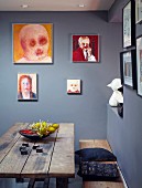 Rustic wooden bench and table below portraits on grey-blue walls in corner