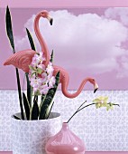Plastic flamingos in potted house plant, pink vase and pink photo mural of clouds