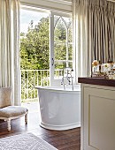 Free-standing vintage-style bathtub next to open balcony door of large, elegant bathroom