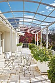 French bistro furniture and planters on sunny terrace below curved metal pergola below blue sky